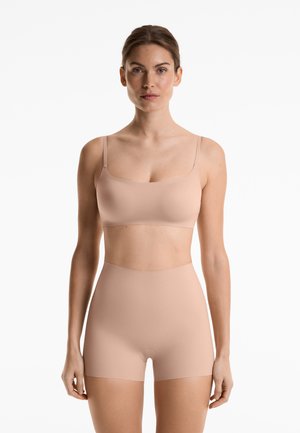 Beige seamless bra with thin straps paired with matching high-waisted shorts. Made from soft, smooth fabric. Minimal design and stretchable fit.