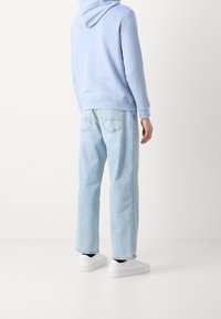 Světlounce modrá mikina s kapucí, doplněná volnými světlounce modrými džínami a bílými teniskami s černými detaily. Hladká textura látky.