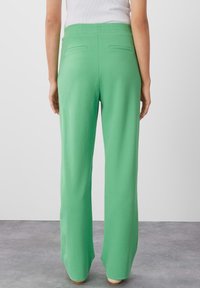 Groene wijde broek met een gestructureerde afwerking, featuring een hoge taille en twee achterzakken, getoond van achteren tegen een neutrale achtergrond.