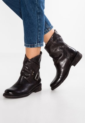Bottines en cuir noir avec boucle latérale portées avec un jean court bleu sur fond blanc.
