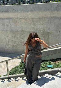 Szary zestaw dwuczęściowy w prążek, składający się z bezrękawnikowego topu i spodni z szerokimi nogawkami. Dodatki obejmują małą czarną torebkę. Tło w kolorze betonu.