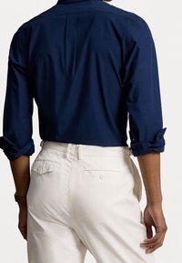 Marineblaue Langarm-Hemden mit umgeschlagenen Manschetten, kombiniert mit cremefarbenen Chinos, die über eine Gesäßtasche und dezente Steppdetails verfügen.