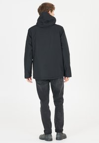 Sort hættejakke med en glat tekstur, forlommer og en afslappet pasform. Kombineret med sorte denimjeans og grå fodtøj.