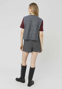 Gilet en tricot gris sur une chemise bordeaux, associé à un short gris et des bottes noires montant jusqu'aux genoux. Textures lisses, design décontracté.