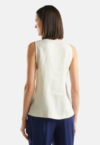 Top senza maniche di un beige chiaro con vestibilità ampia, realizzato in tessuto di lino. Presenta un colletto rotondo e una trama sottile. Abbinato a pantaloni blu navy.