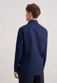 Camicia a maniche lunghe blu navy in tessuto liscio, con collo classico, polsini con bottoni e orlo curvo, vista da dietro.