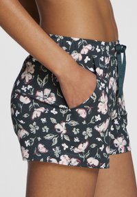 Bloemmotief shorts van donkergroen stof met een trekkoord in de taille, twee zijzakken en een zachte textuur met roze en witte bloemen.