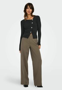 Haut à manches longues noir côtelé avec un décolleté carré et cinq boutons argentés, associé à un pantalon olive vert ample et des chaussures noires.