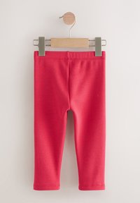 Red toddler leggings with elastic waistband hanging on wooden hanger against white background.