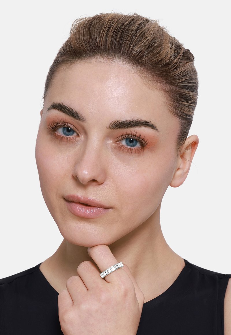 Anello in argento con gemme trasparenti rettangolari incastonate in una fascia dritta. Modella in posa con la mano sul mento, indossando un top nero.