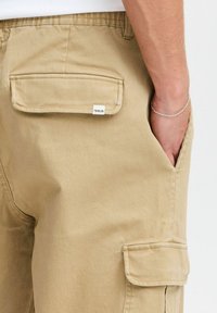 Khaki cargobroek met een rechte snit, voorzien van zijzakken, een achterzak met klep en een klein merketiket. Gestructureerde katoen stof.