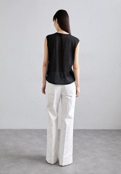 Schwarzes ärmelloses Oberteil mit transparenter Textur und abgerundetem Saum, kombiniert mit weißen weit geschnittenen Hosen mit Gesäßtaschen.