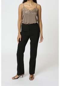 Ruskea satiinihihaton paita, jossa on pitsireunus, yhdistetty mustiin räätälöityihin housuihin ja mustiin korkokenkiin. Sujuva pinta ja tyylikäs muotoilu.