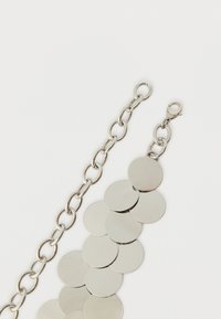 Brățară din lanț argintiu cu discuri rotunde din metal lustruit și închizătoare tip caracatiță. Linkuri texturate și elemente circulare netede creează un contrast vizual.