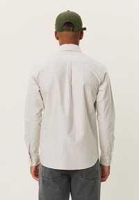 Lichtgekleurde, verticaal gestreepte shirt met lange mouwen en een klassieke kraag. De stof lijkt glad; de achterkant heeft een centrale plooi.