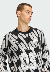 Černá a šedá vzorovaná košile s dlouhým rukávem a límečkem, s logem "adidas", číslem "03" a kulatou nášivkou na hrudi.
