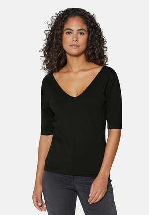 Schwarzes V-Ausschnitt-Oberteil mit kurzen Ärmeln, aus einem weichen Stoff; figurbetontes Design mit glatter Textur, kombiniert mit dunkelgrauen Jeans.