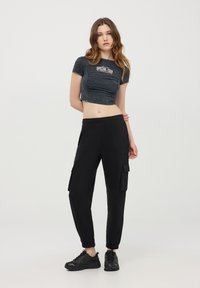 Pantaloni cargo neri con polsini elastici alle caviglie, abbinati a una t-shirt grigia cropped con il testo "SPECIAL TOUR". Indossati con scarpe da ginnastica nere.