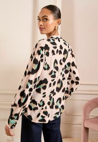 Blusa leggera a maniche lunghe in rosa pallido con stampa leopardata nera e verde petrolio. Presenta polsini con bottoni e una vestibilità comoda.