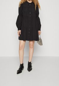 Black button-up dress with tiered design, long puff sleeves, and gathered details. Pair of black ankle boots with pointed toes and decorative hardware.