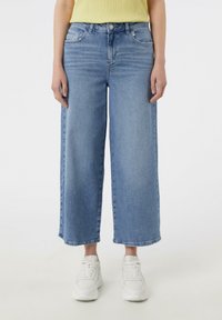 Světle modré široké džíny vyrobené z denimu, s vysokým pasem, pěti kapsami a surovým lemem. Spárované s bílými teniskami.