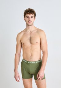 Green boxer shorts with a white "BJÖRN BORG" waistband, fitted design, cotton blend material, and smooth texture. Model displays front view.