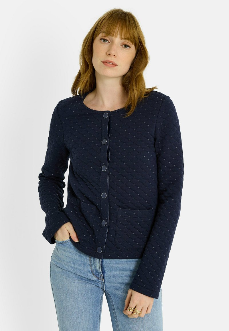 Chaqueta acolchada azul marino con escote redondo, cierre de botones, dos bolsillos frontales y patrón texturizado. Mangas largas con puños doblados.