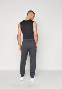 Sort ærmeløs top parret med grå sweatpants med elastisk liv og opkrøllede ankler, modelleret fra ryggen. Hvide sneakers inkluderet.