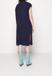 Abito lavorato a maglia blu navy con colletto alto e spacchi laterali, abbinato a stivali da cowboy azzurri chiari con dettagli ricamati e punta affusolata.