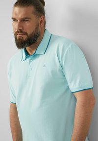 Jasnoniebieska koszula polo wykonana z bawełny, z kołnierzykiem w kontrastowym ciemnoniebieskim kolorze, dwoma guzikami oraz małym logo na piersi.