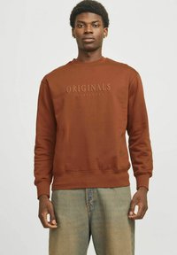 Sudadera marrón con cuello redondo, puños y dobladillo acanalados. Presenta el texto en relieve "ORIGINALS JACK & JONES" en el frente. Textura de tela suave.