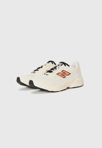O pereche de adidași New Balance de culoare crem, cu șireturi negre și logo portocalie, pe un fundal alb, înclinați spre dreapta.
