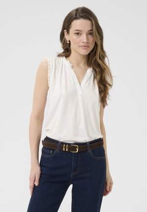 Haut sans manches blanc avec un col froncé, associé à un jean bleu foncé et une ceinture marron avec une boucle en or.