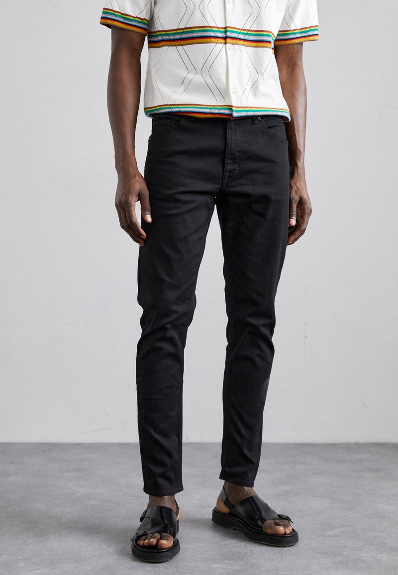 Jeans hitam slim-fit terbuat dari denim, dengan desain lima kantong klasik. Dipadukan dengan sandal hitam dan kemeja lengan pendek multicolor.