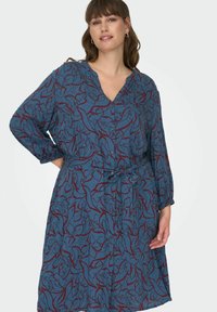 Robe bleue avec un motif floral bordeaux. Décolleté en V avec fermeture à boutons et taille ceinturée. Manches longues avec poignets élastiques.