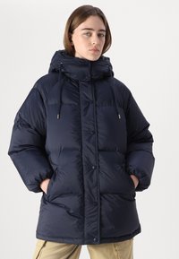 Marinblå puffjacka med huva, med en boxig design, tryckknappsstängning, framfickor och dragsko för justerbar passform.