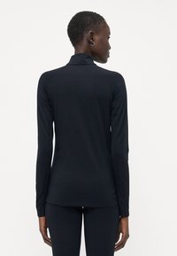 Bluză cu mânecă lungă, ajustată, de culoare neagră, confecționată dintr-un material ușor. Dispune de un guler înalt și un design fără cusături la umeri pentru o siluetă fluidă.
