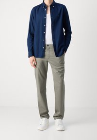 Chemise à boutons navale sur un débardeur blanc, associée à un pantalon gris clair et des baskets blanches. Coupe décontractée avec un tissu lisse et un col standard.