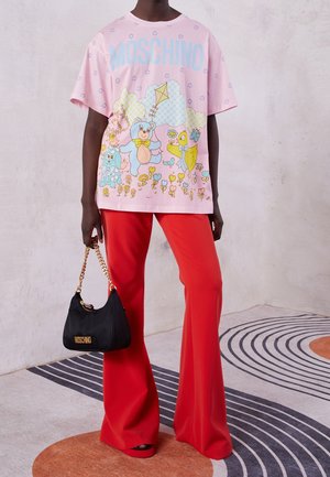 Osoba nosząca różowy t-shirt Moschino z nadrukiem misia, jasnoczerwone szerokie spodnie i trzymająca małą czarną torebkę Moschino z złotym łańcuszkiem.