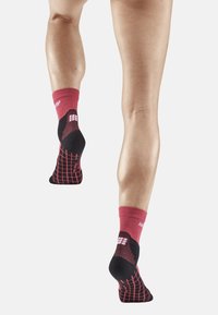 Calze compressive nere e rosse con un motivo a griglia e supporto alla caviglia testurizzato, progettate per l'uso atletico, mostrate sulle gambe di una persona.