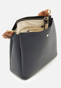 Marinblå läderväska med en strukturerad form, med bruna knutna handtag och en guldfärgad dragkedja. Inuti är den fodrad med lätt tyg och har fickor.