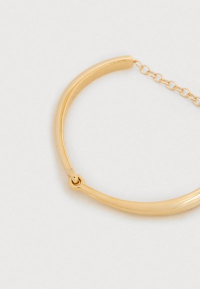 Bracelet ton doré avec un design lisse et arrondi. Il dispose d'un fermoir sécurisé et d'un petit accent de cha îne. Apparence minimaliste et élégante.