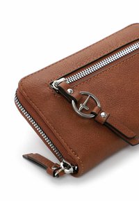 Portefeuille en cuir texturé marron avec une fermeture éclair argentée, un accent de matériel circulaire et un design épuré. Forme compacte et multifonctionnelle.