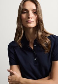 Polo shirt blu navy con bottoni, maniche corte e colletto a costine. Tessuto liscio con un design aderente.