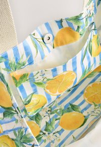 Canvas tote bag with a blue and white striped interior featuring lemon and floral patterns; includes a snap button closure and textured fabric.