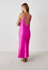 Vestido de tirantes finos en satén rosa con un diseño de espalda baja, con un dobladillo recto que roza el suelo. Textura suave y lisa.