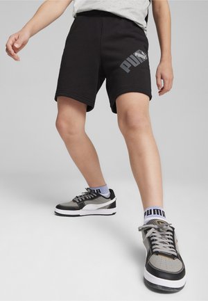 Corti di cotone neri con logo PUMA; accentuazione in grigio. Sneakers nere e grigie con suola bianca e calzini a righe completano l'outfit.