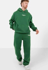 Felpa verde con cappuccio e pantaloni abbinati in morbido pile. Caratterizzata da tasca frontale e testo del logo bianco sul petto e sulla gamba. Vestibilità comoda.