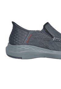 Zapato slip-on gris pizarra con upper de tejido texturizado, suela de goma moldeada y un sutil detalle en rojo del logo en el lateral.