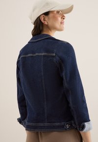 Jeansjacka med mörkblå tvätt, knappade ärmslut och kontrasterande ljusa denimdetaljer på ärmarna. Har klassisk krage och skräddarsydd design.